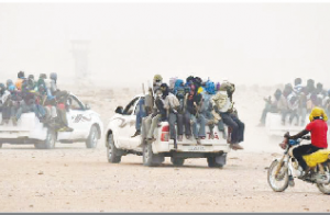Migrants sit on the open cargo of pick-up trucks, holding wooden sticks tied to the vehicle to avoid falling from it, as they leave the outskirts of Agadez for Libya (AFP)